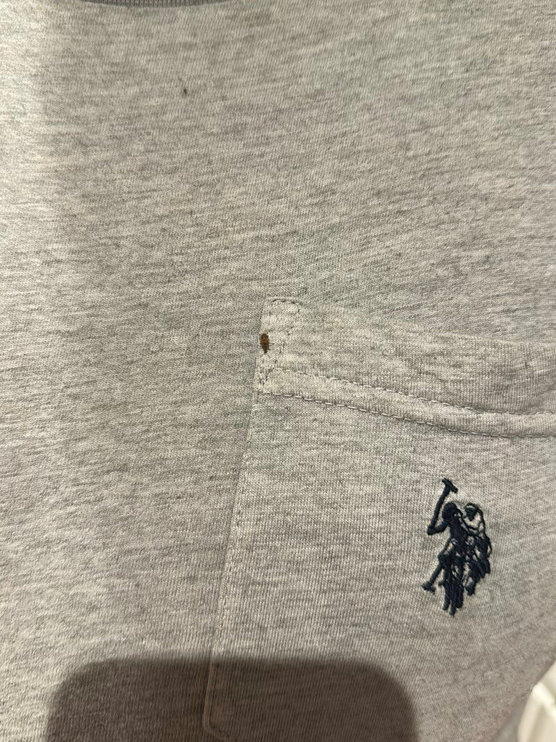 Una singola cimice dei letti è seduta su un tessuto grigio vicino alla cucitura della tasca di una camicia. Il piccolo insetto è chiaramente visibile.