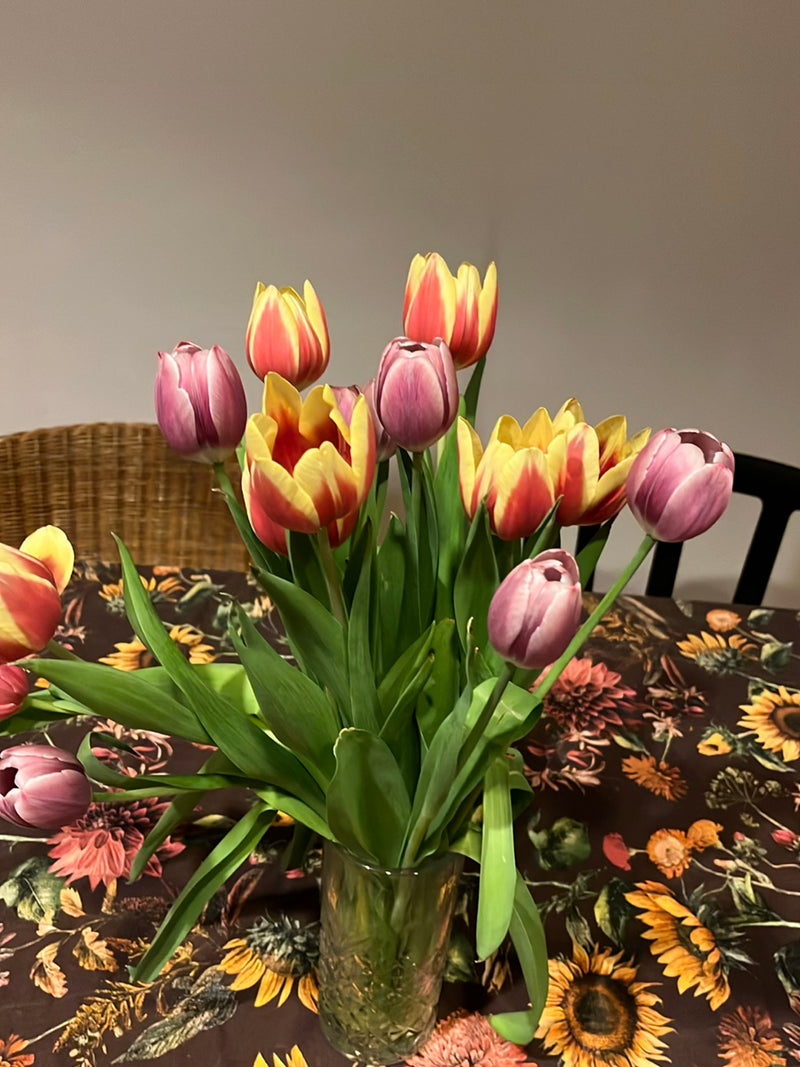 Un colorato bouquet di tulipani da giardino si trova in un vaso di vetro su un tavolo decorato. I fiori mostrano vari colori come rosso, giallo e rosa.