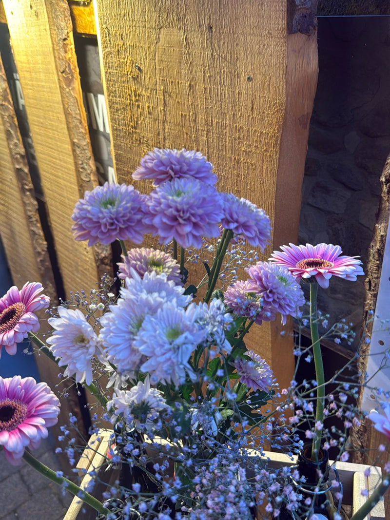 Si vede un colorato bouquet di fiori con gerbere e altri fiori di fronte a una parete di legno. Le piante sono in contenitori.