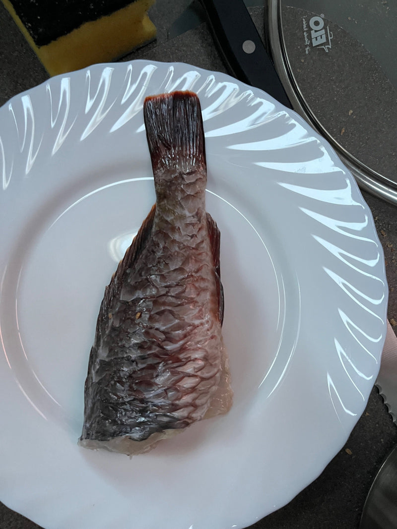 Un pezzo di carpa con scaglie ben visibili e la pinna caudale si trova su un piatto bianco.