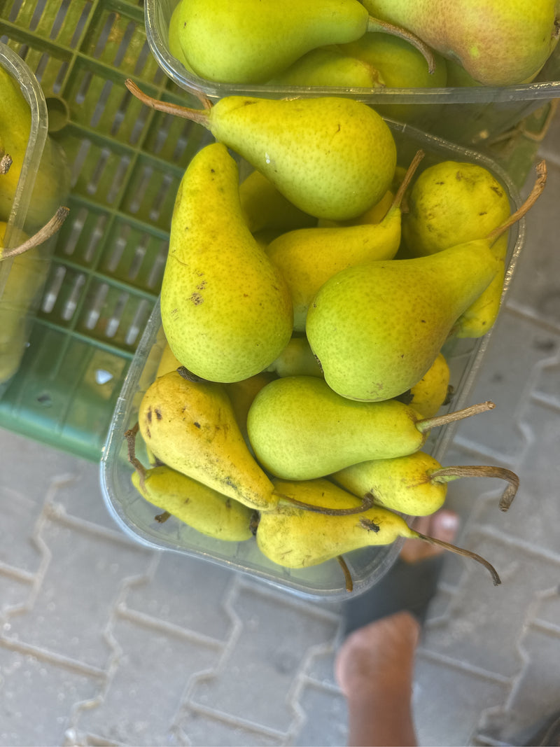 Diverse pere nashi mature si trovano vicine in un vassoio di plastica. I frutti giallo-verdi sono chiaramente visibili dall'alto.