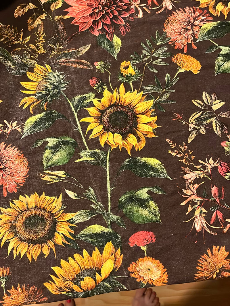 Il motivo del tessuto raffigura diversi girasoli gialli con centri scuri e foglie verdi. L'illustrazione mostra varie infiorescenze su uno sfondo marrone.